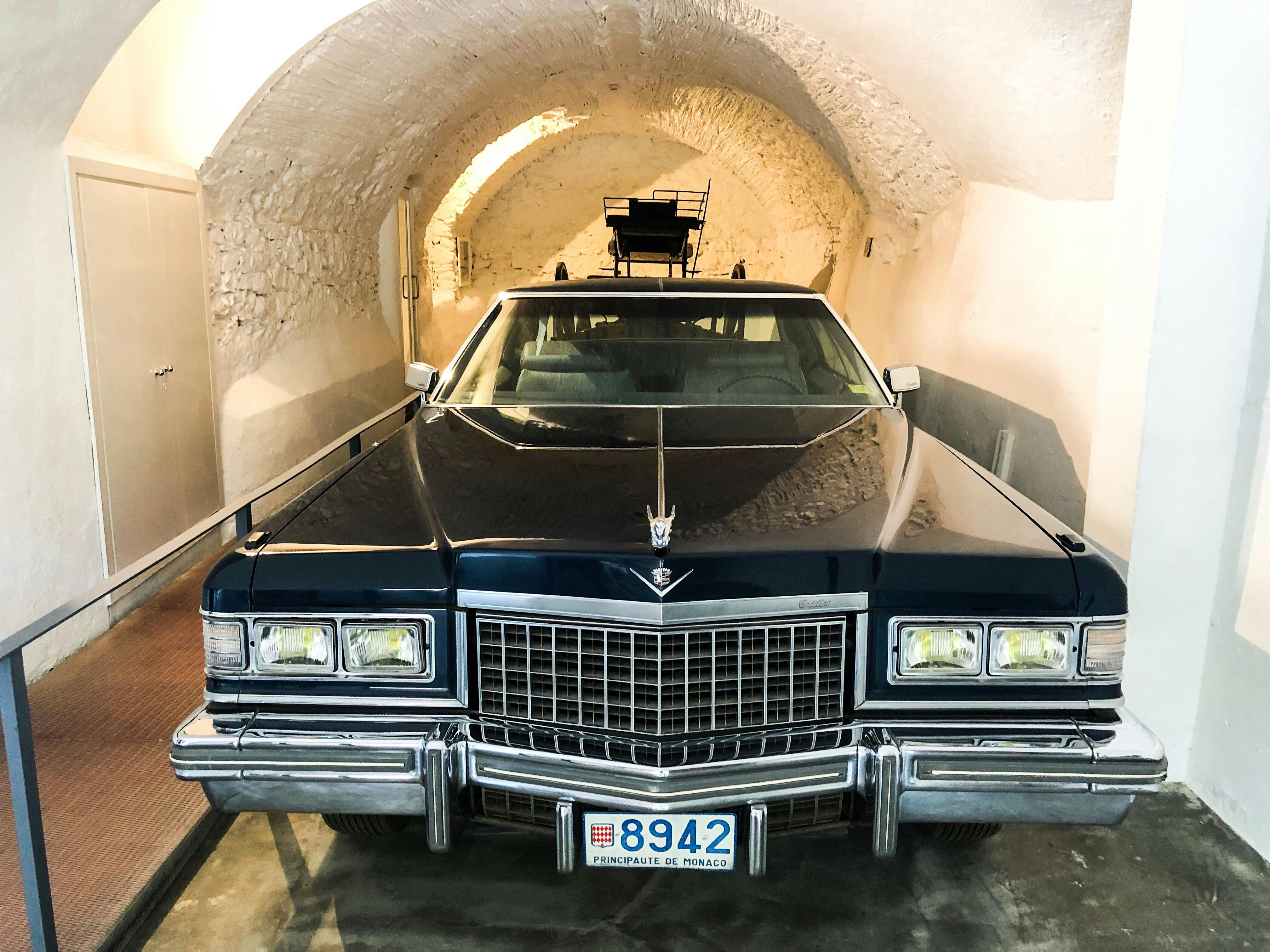 モナコのナンバープレートを備えたクラシックな青いキャデラックは、アーチ型の石造りの天井を備えたトンネルのようなガレージに駐車されています。