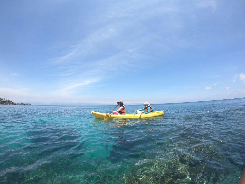 Two people in life vests paddle a yellow kayak on clear blue water under a sunny sky.