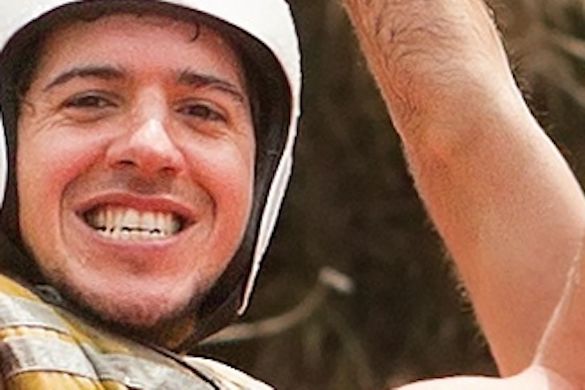 Four people in helmets and life vests celebrate while white-water rafting in an orange inflatable boat on a river.