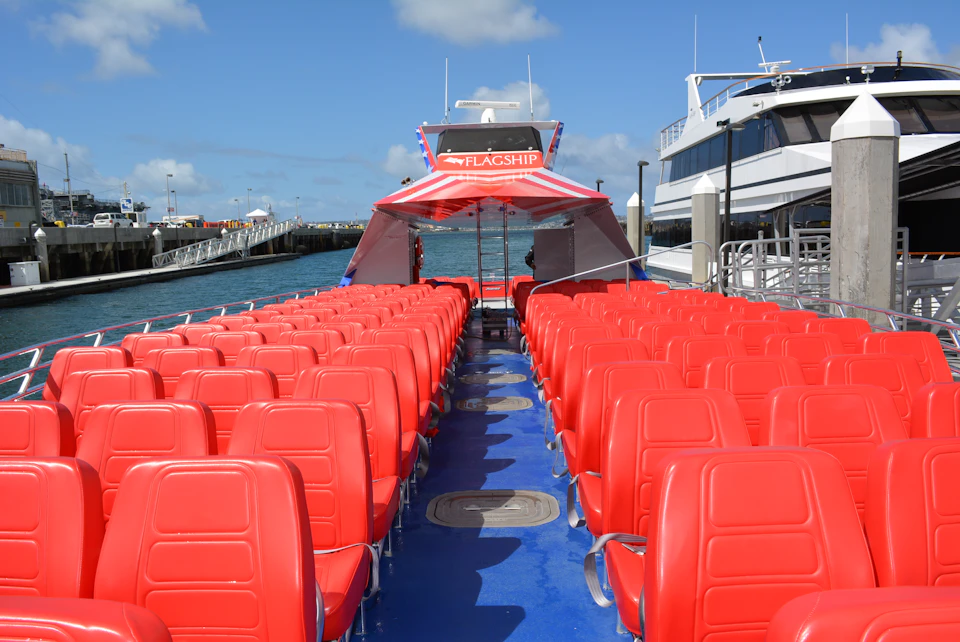 Rows of red seats on a boat deck labeled "FLAGSHIP," docked beside another boat under a blue sky.
