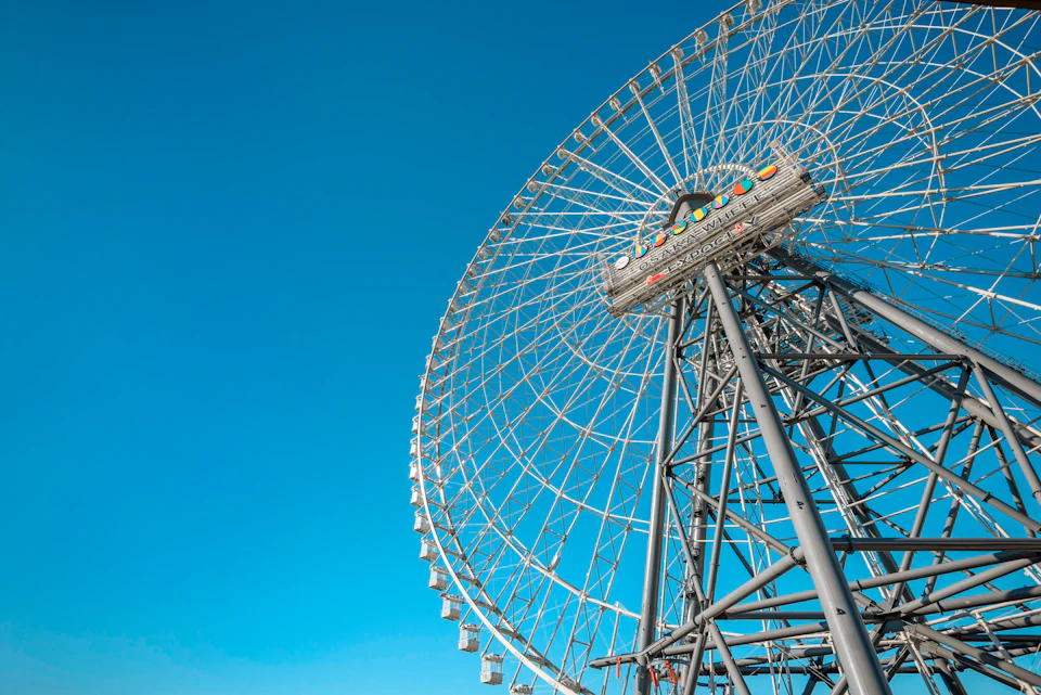 A large ferris wheel with colorful gondolas against a clear blue sky, viewed from below at an angle.