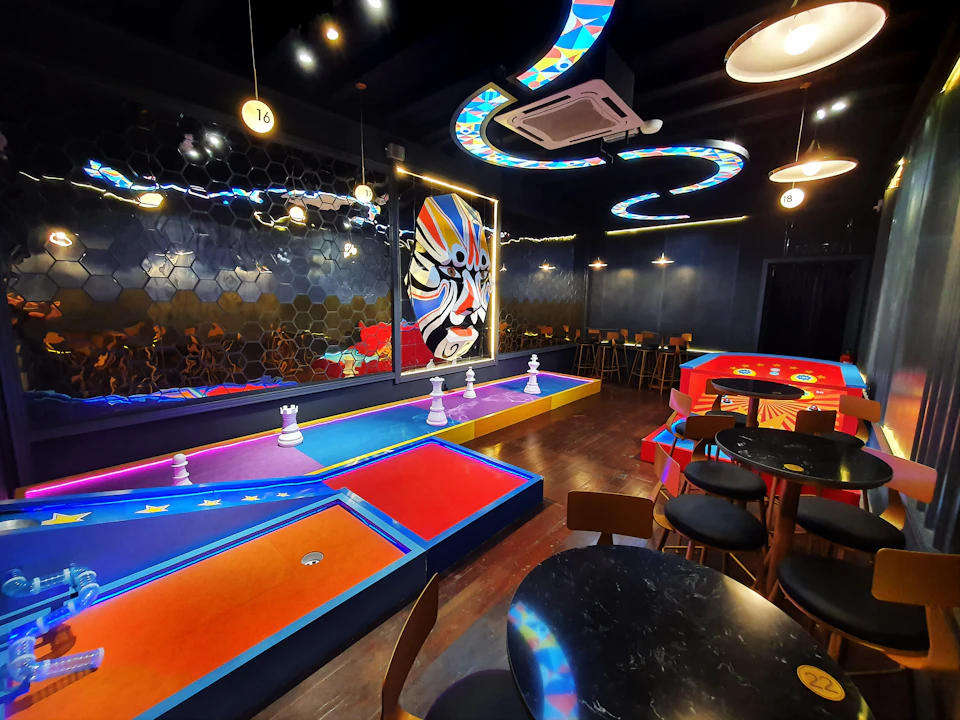 A vibrant indoor mini-golf setup with colorful decor, abstract wall art, and modern furniture under dramatic lighting.