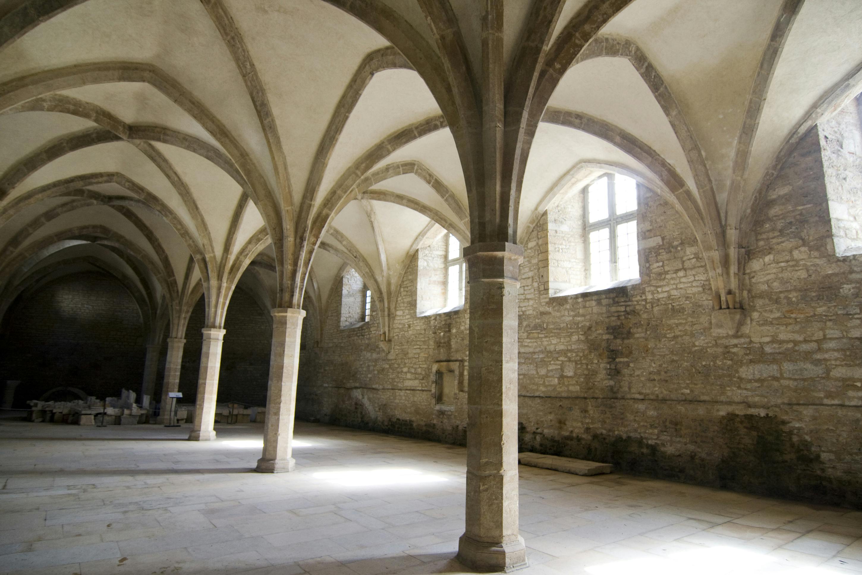 高いアーチ型の天井、いくつかの柱、大きな窓がある石造りのホール。 光が流れ込み、空間を照らします。