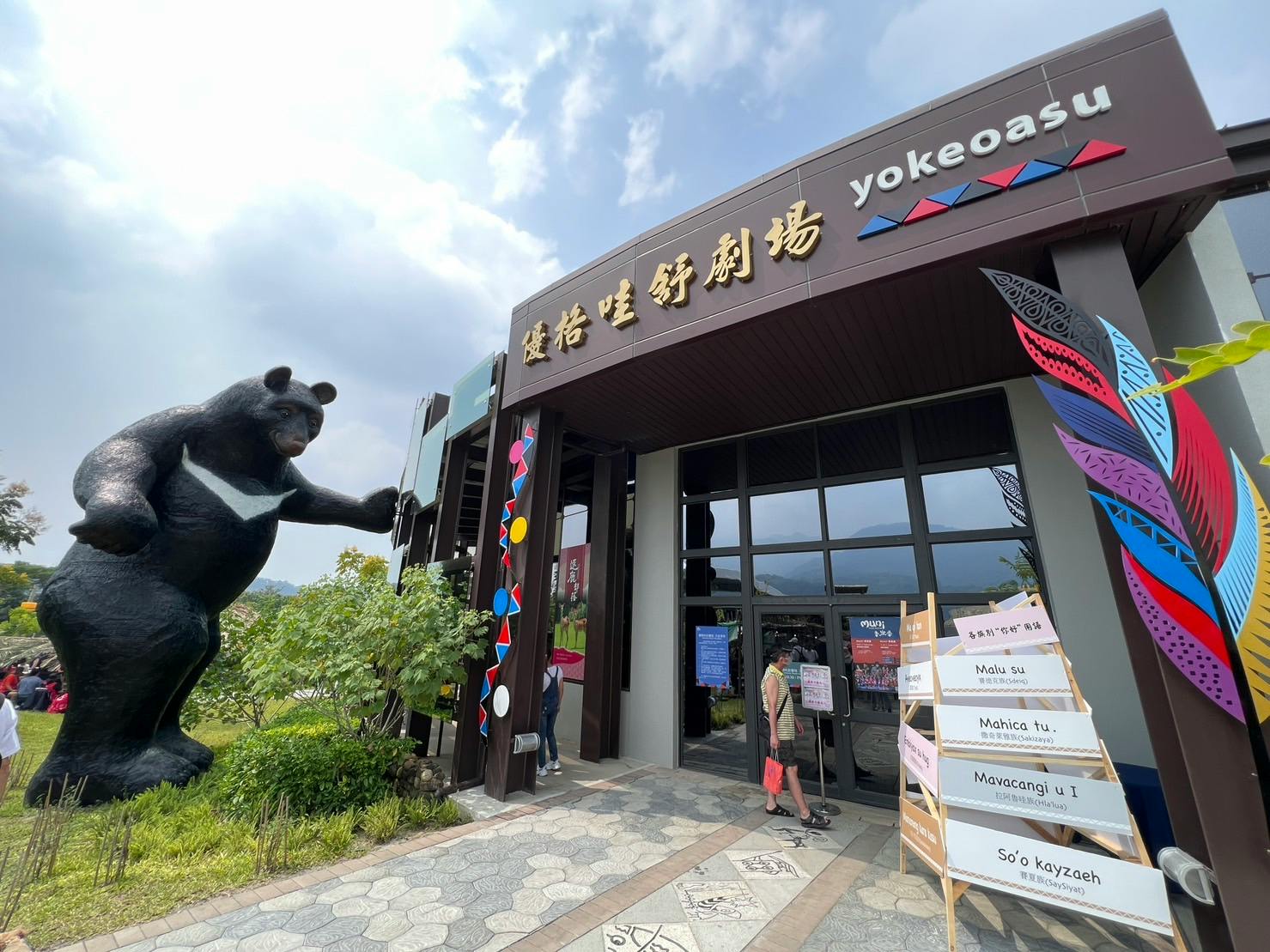 Building entrance with a bear statue and colorful decorations. A signboard with text is displayed near the entrance.