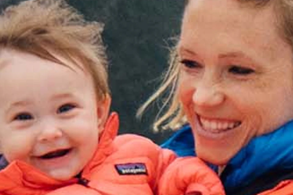 A woman holding a smiling baby on a boat with a scenic background of mountains, water, and mist.