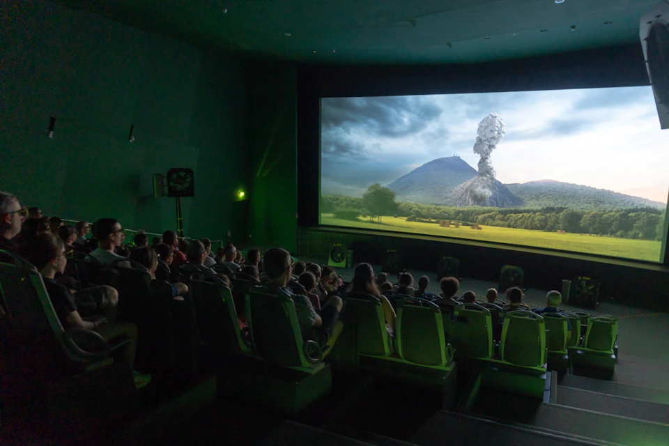 People sitting in a dark theater watching a movie scene featuring a volcanic eruption in a landscape.