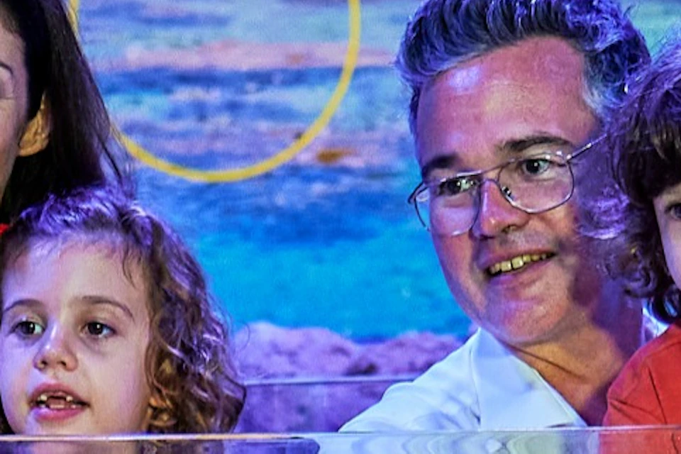A family of four smiles near an aquarium exhibit featuring shallow water marine environments with colorful coral and fish.