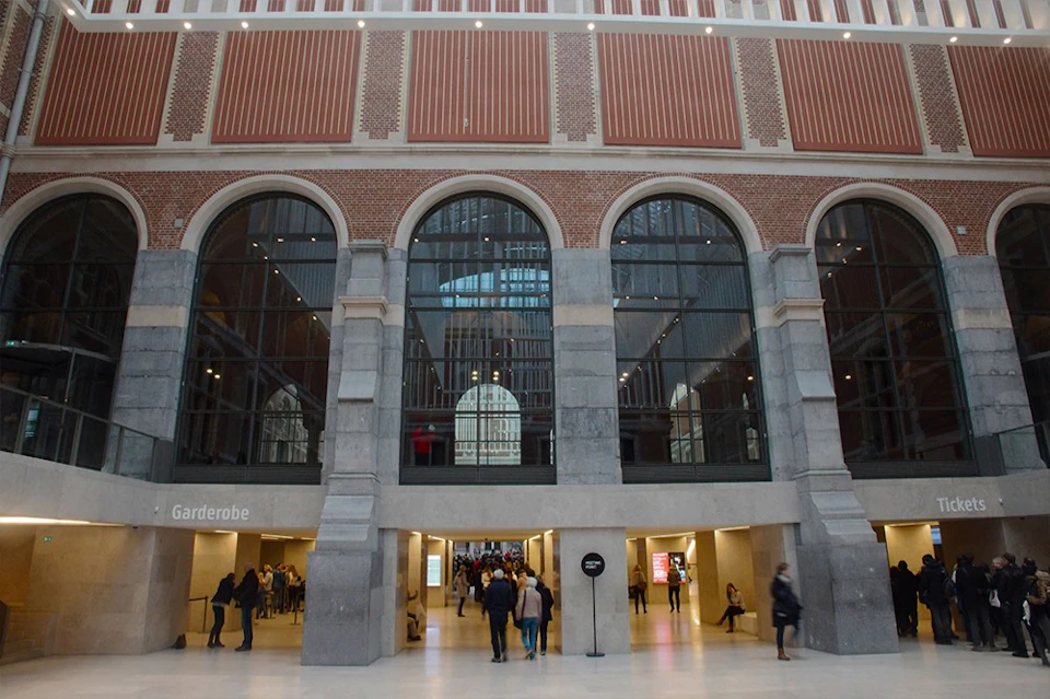 People walking through the entrance of a building with large arched windows and brick walls, featuring high ceilings and modern lighting.