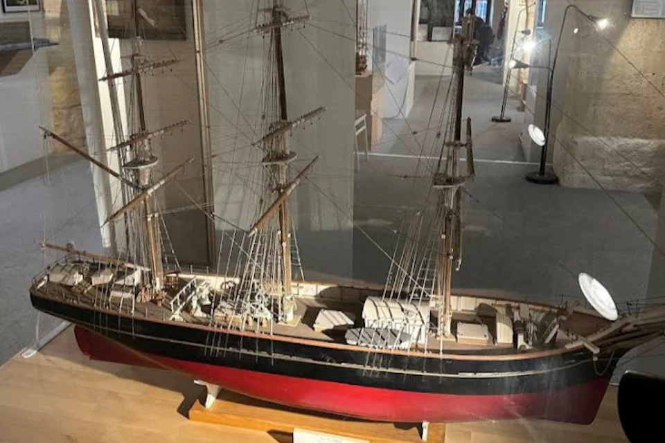 A detailed model of a sailing ship with three masts displayed in a glass case in a museum setting.