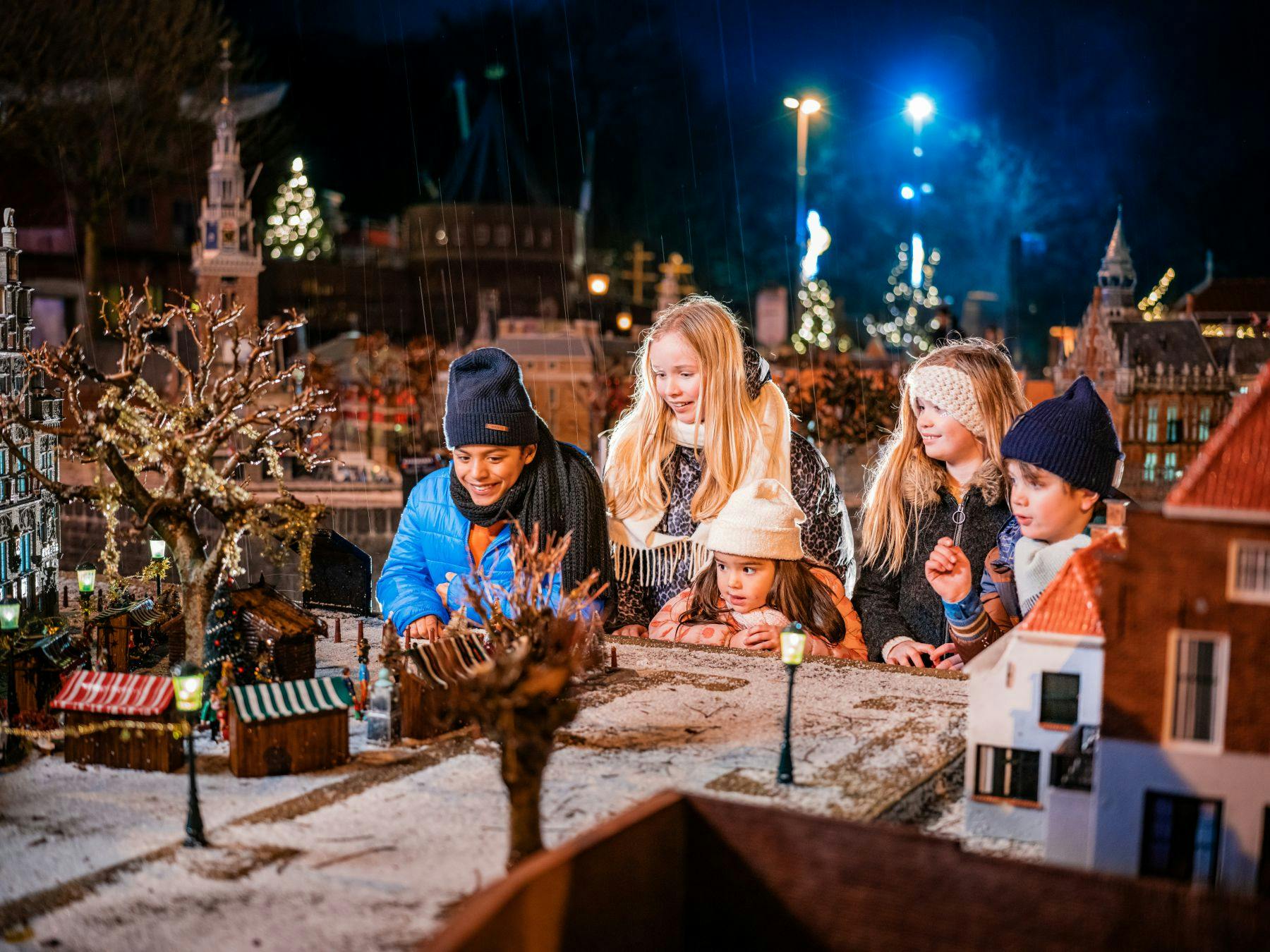 冬の服を着た5人の子供たちが、夜にライトアップされたミニチュアの町を探検します。