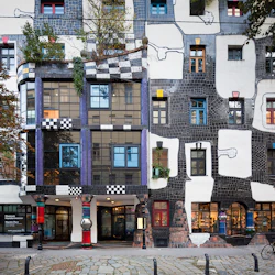 Färgglad, eklektisk byggnadsfasad med oregelbundet formade fönster, livfulla pelare, mosaikmönster och takgrönska.