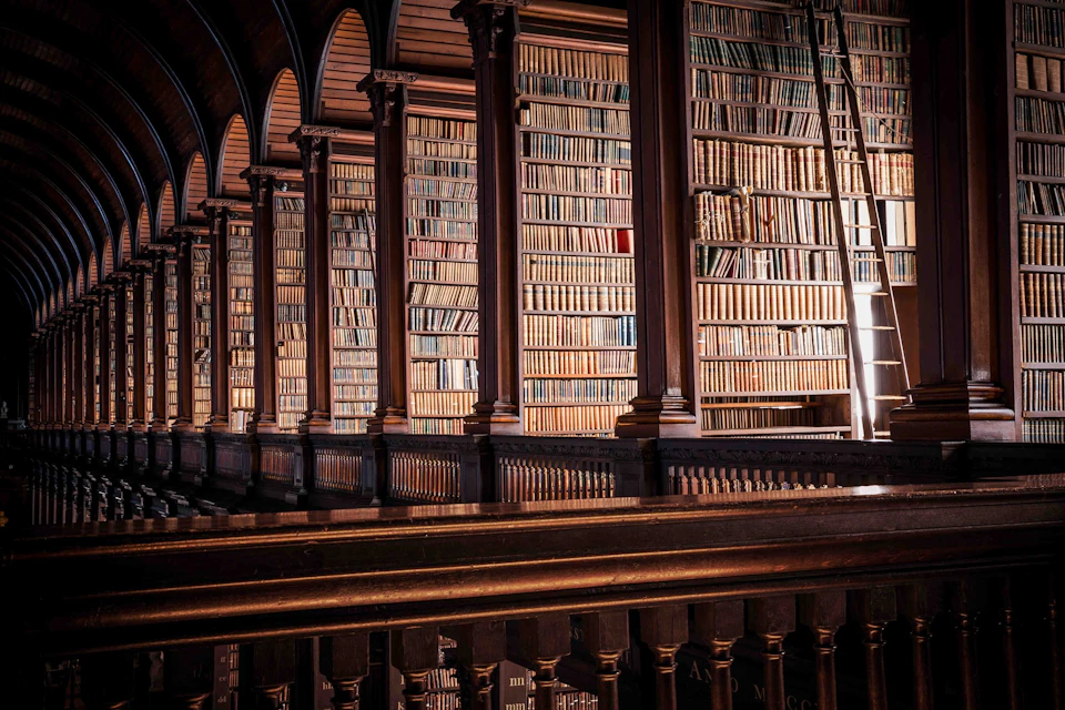 An ornate library with tall wooden bookshelves, filled with numerous books, separated by dark wooden arches and columns.