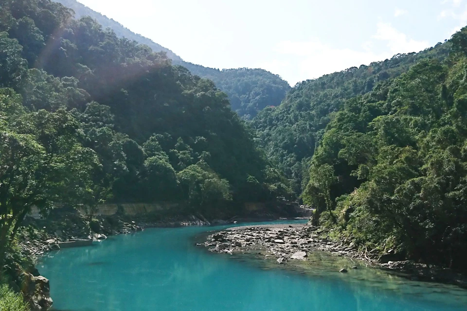 A serene turquoise river surrounded by lush green forested hills under a bright sky.