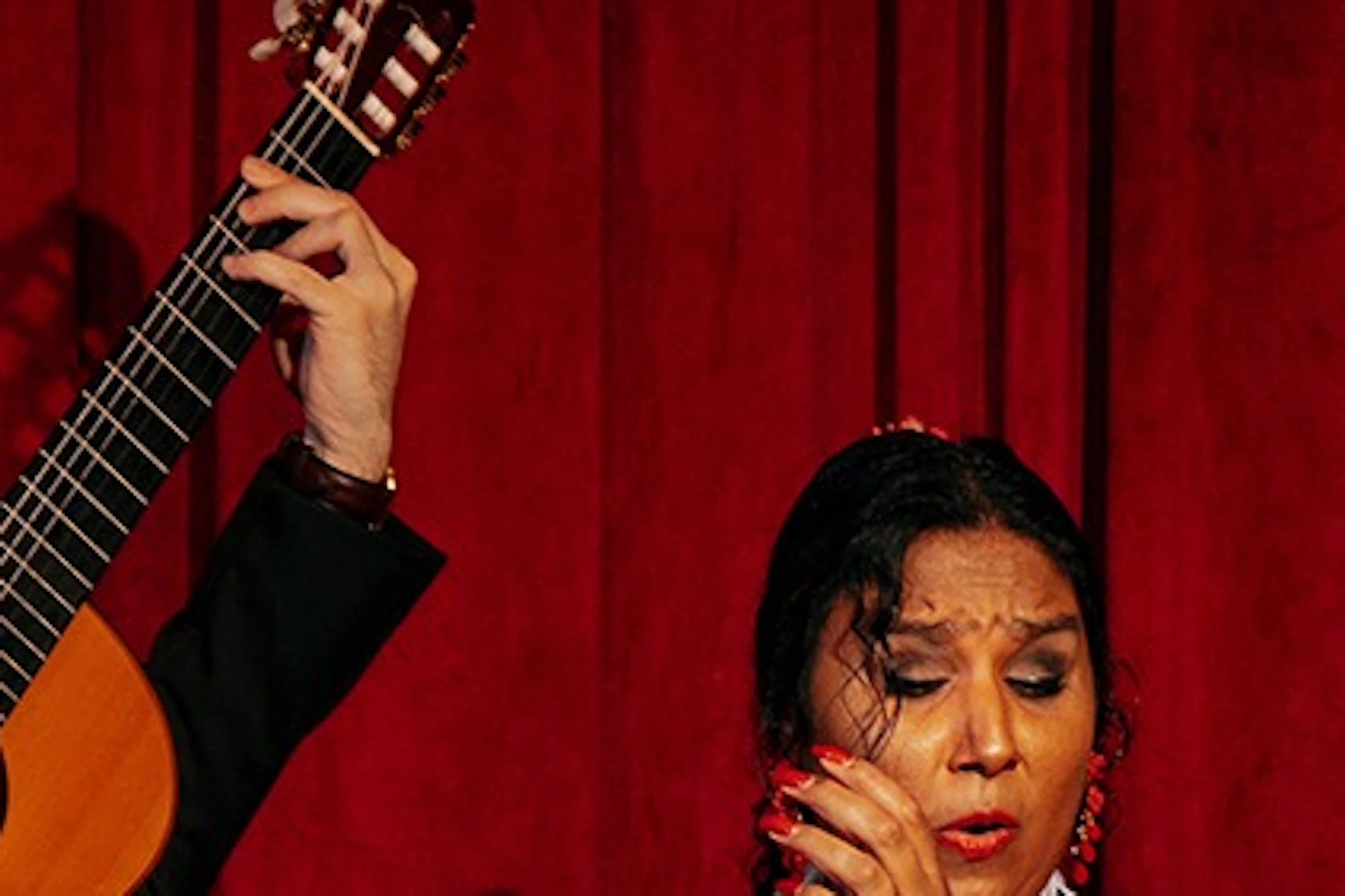 Flamenco dancers in vibrant red outfits performing beside musicians against a red curtain backdrop.