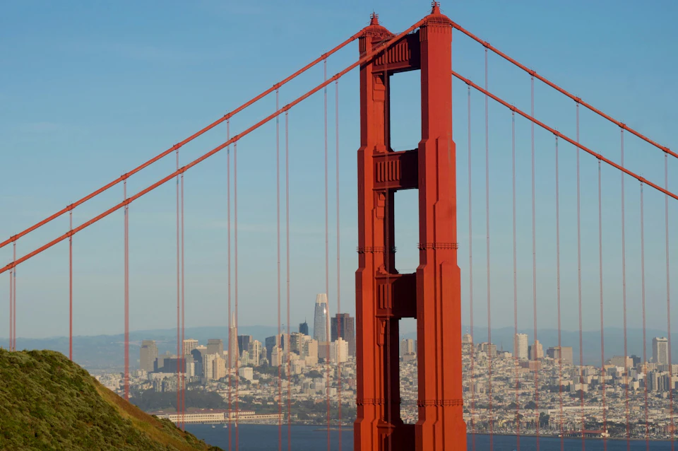 Close-up view of the Golden Gate Bridge's tower with the skyline of San Francisco visible in the background.