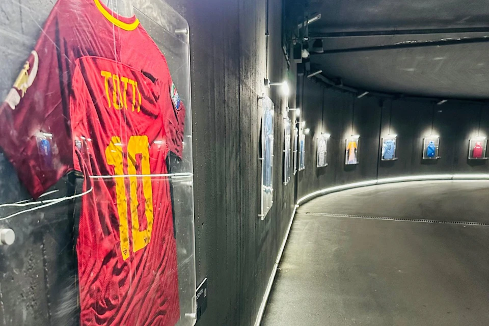 A dimly lit hallway with framed sports jerseys on the wall, including a red jersey with "10 Totti" visible in the foreground.