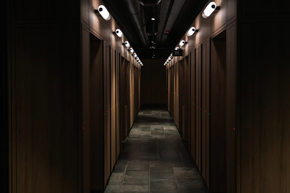 Dimly lit hallway with wooden lockers on both sides and overhead lights.