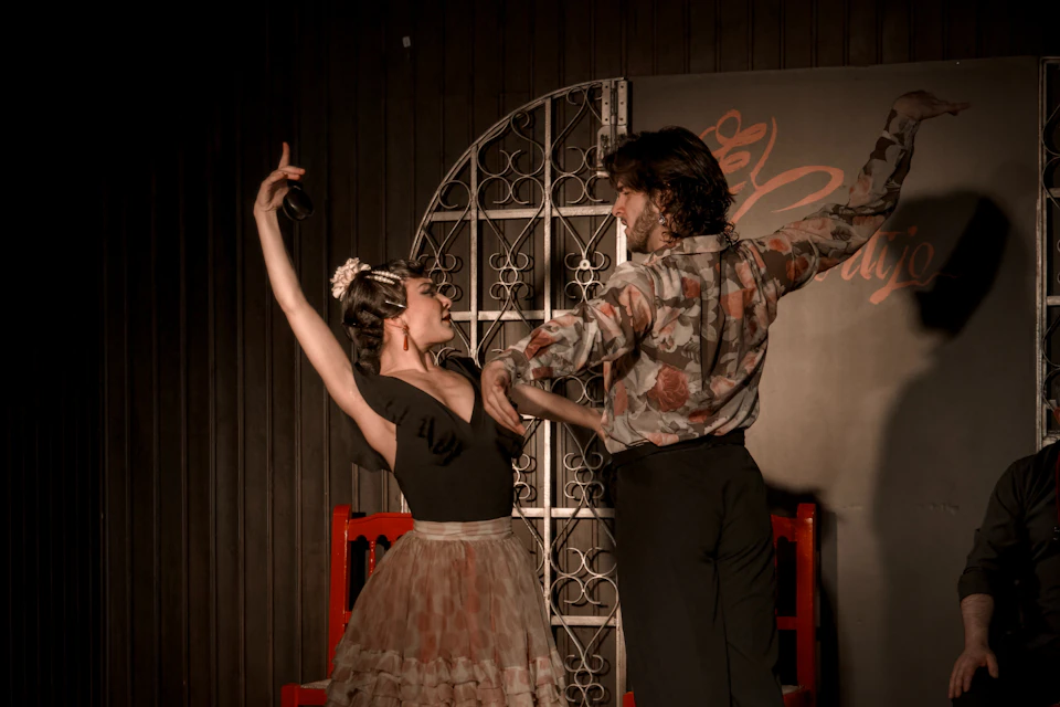 A man and a woman are performing a flamenco dance on stage; the woman is holding castanets and wearing a traditional costume.