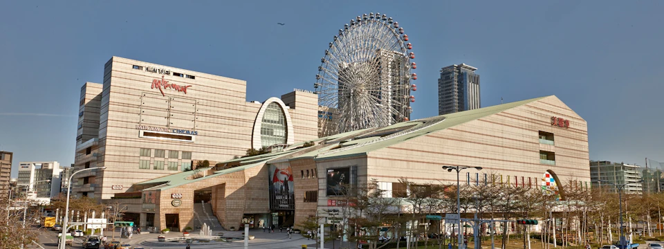 A modern shopping complex with a large Ferris wheel in the background under a clear sky.