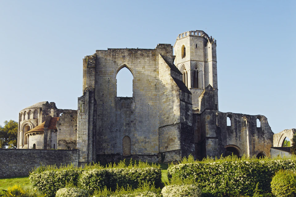 Ancient stone ruins with a tower and arched windows, surrounded by greenery under a clear blue sky.