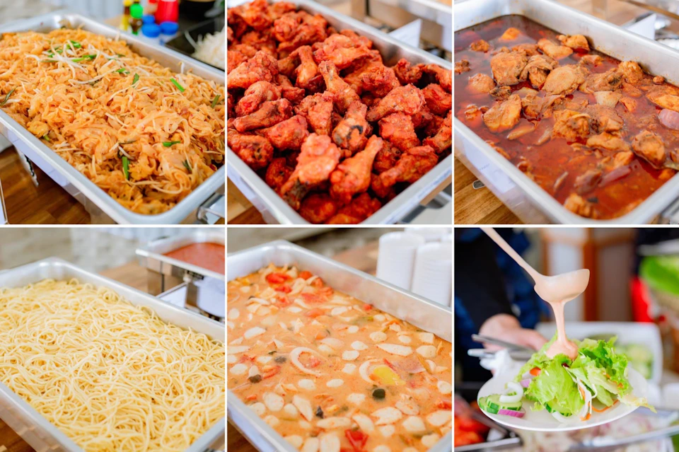 Buffet with various dishes, including fried chicken, pasta, noodles, stew, and salad; condiments visible in the background.