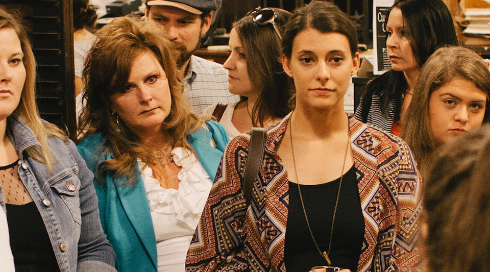 A group of people attentively listening to a speaker in a room with an industrial design and various woodwork pieces visible.