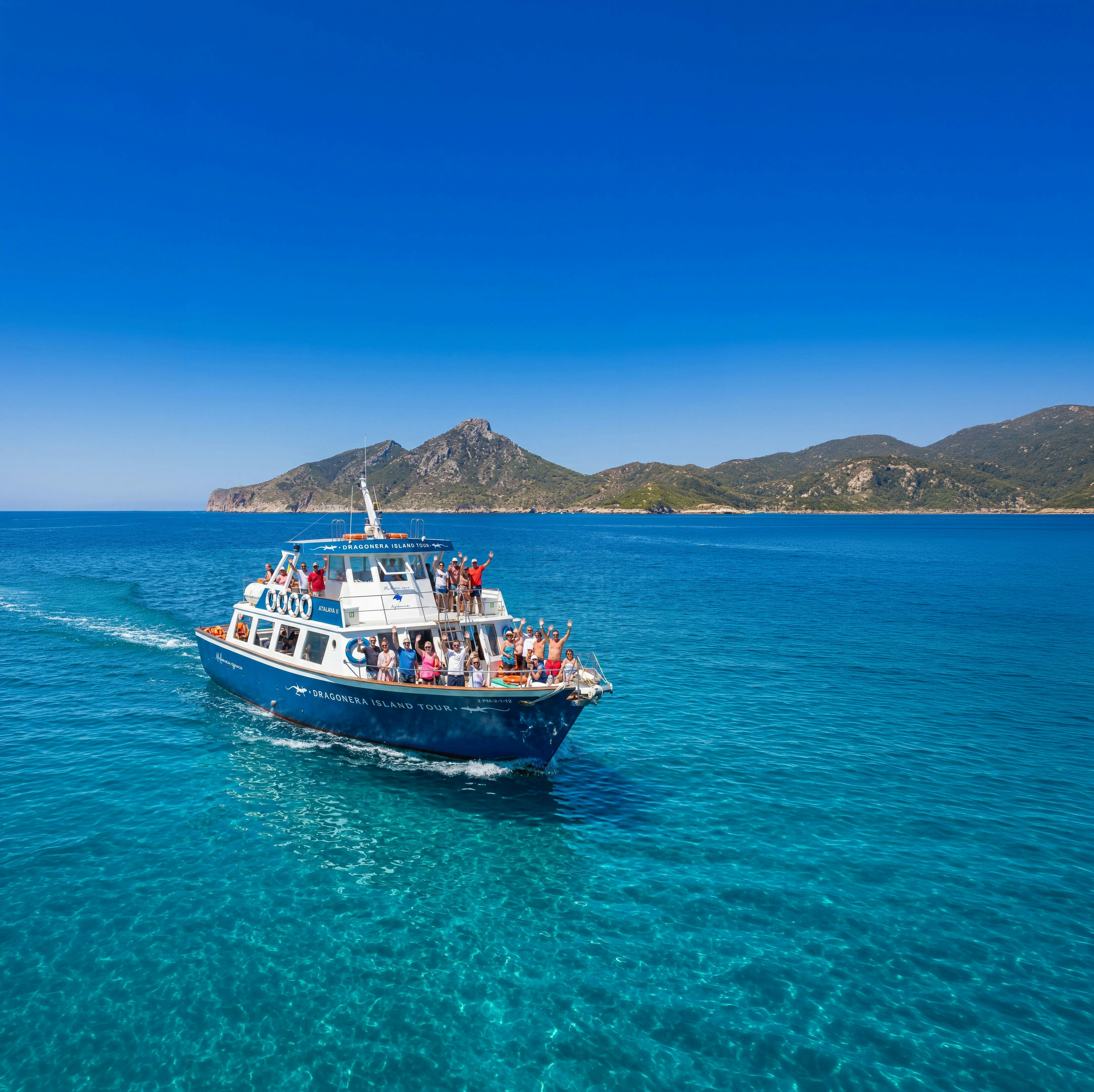 Un tour in barca con persone a bordo naviga in acque limpide e blu sotto un cielo soleggiato, con le montagne visibili sullo sfondo.