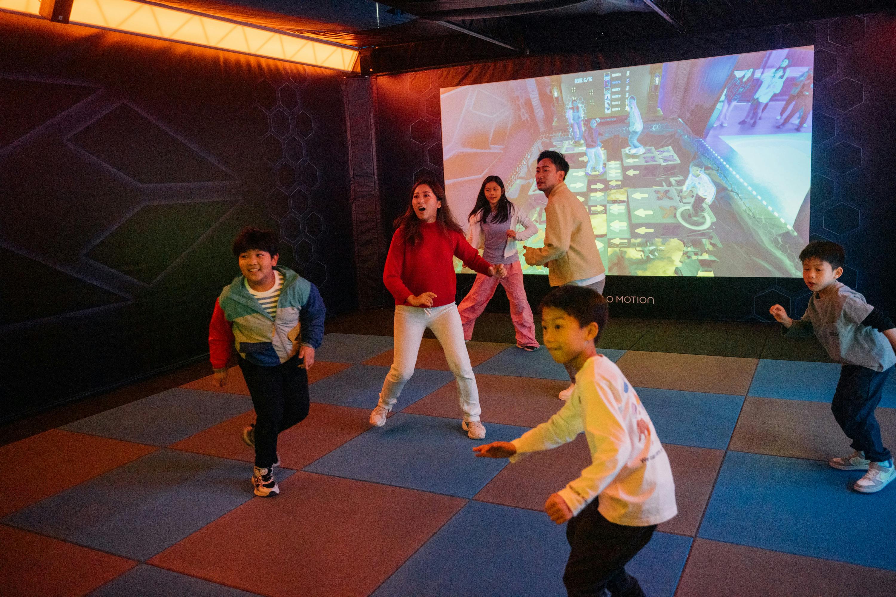 A group of children and adults playing an interactive game in a room with a large projection screen showing graphics.