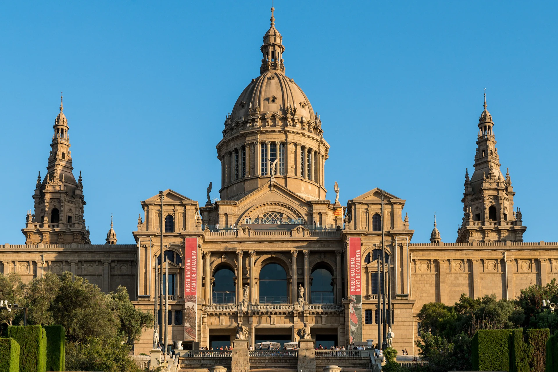 Grand architectural building with a central dome and two towers, featuring banners on the facade and a staircase in the foreground.