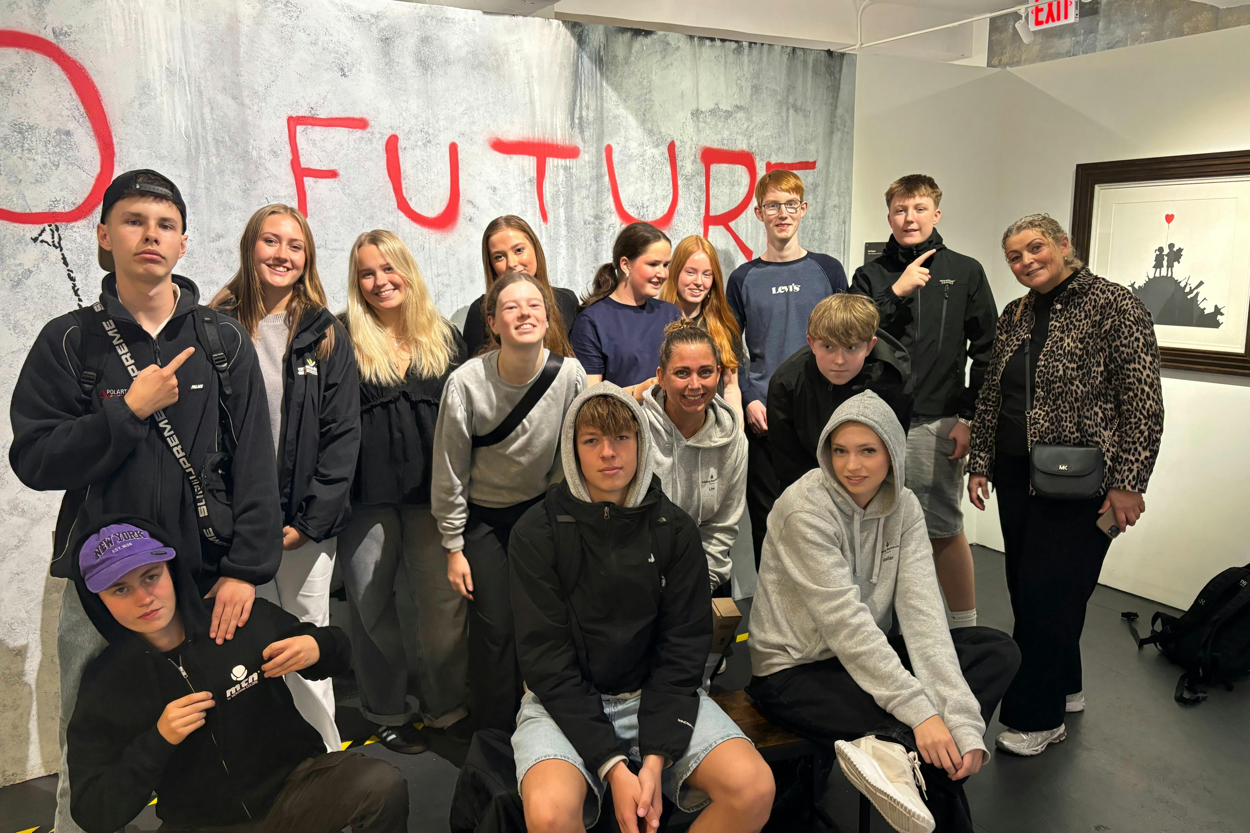 A group of teenagers stands together in front of a wall with the word "FUTURE" spray-painted in red.