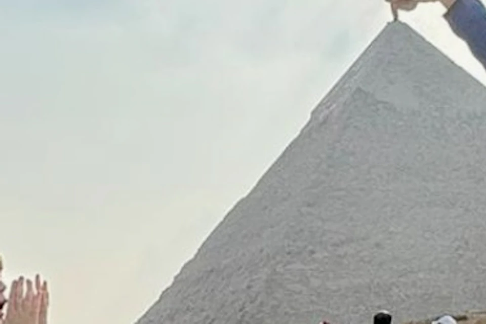 Three people posing as if holding the peak of the Great Pyramid of Giza. Other visitors are visible in the background.