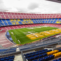 Tom arena med röda och blå säten, gula bokstäver som lyder "mes QUE FN-KLUBB" och ett välskött grönt fält.