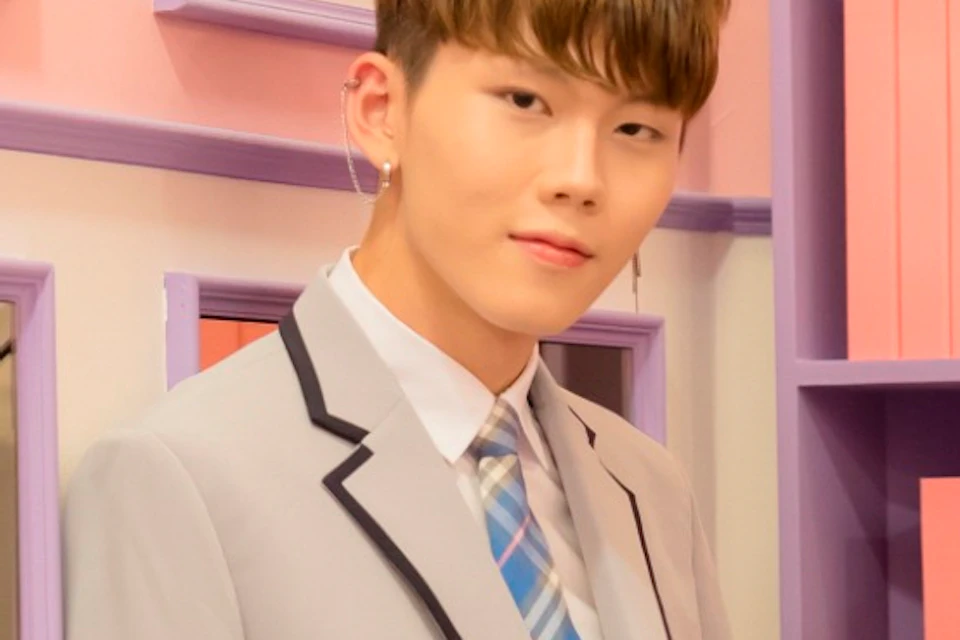 Two people in light gray uniforms stand in a colorful room with pink walls, a mirror, and shelves with pink books.