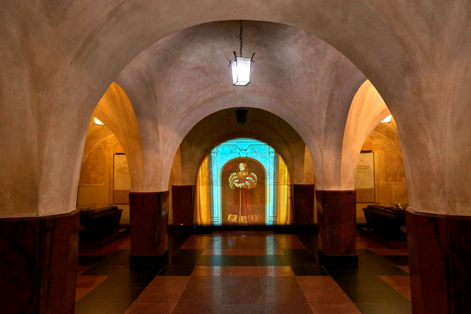 An arched corridor with a lantern hanging from the ceiling. A illuminated image of a historical figure is projected on the far wall.