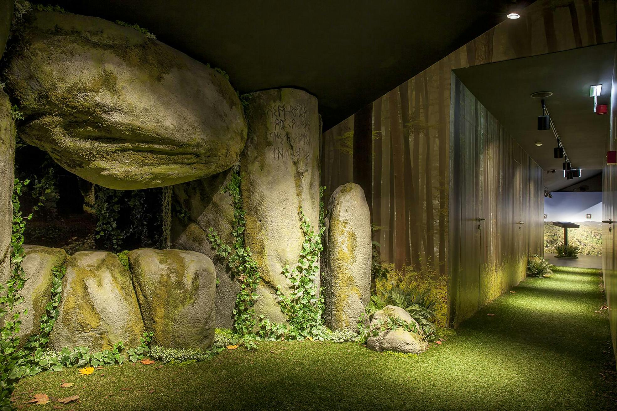 인공 잔디가 깔린 방, 덩굴이 있는 커다란 바위, 숲 장면의 벽지. 오른쪽에 문이 보입니다.