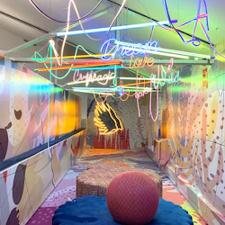 En levande, neonupplyst hall med färgglada fototapeter, mönstrade golv och olika neonskyltar hängande ovanför.