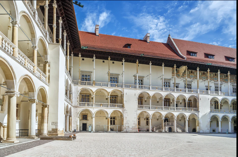 A courtyard with arcade-style architecture, containing multiple arches and columns, under a red tiled roof against a blue sky.