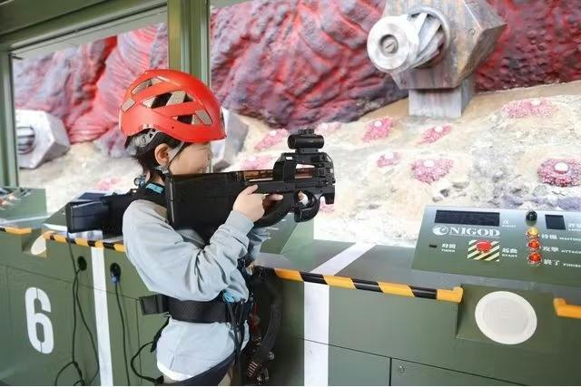 A person wearing a red helmet is holding a toy gun in a themed setting with sci-fi decor and interactive equipment.