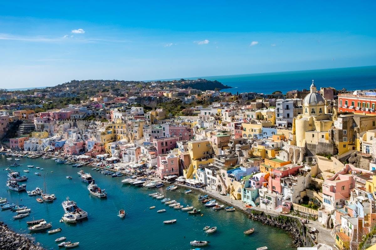 파스텔톤 건물, 항구에 정박한 보트, 맑고 푸른 하늘이 있는 다채로운 해안 마을. 언덕과 바다를 배경으로.