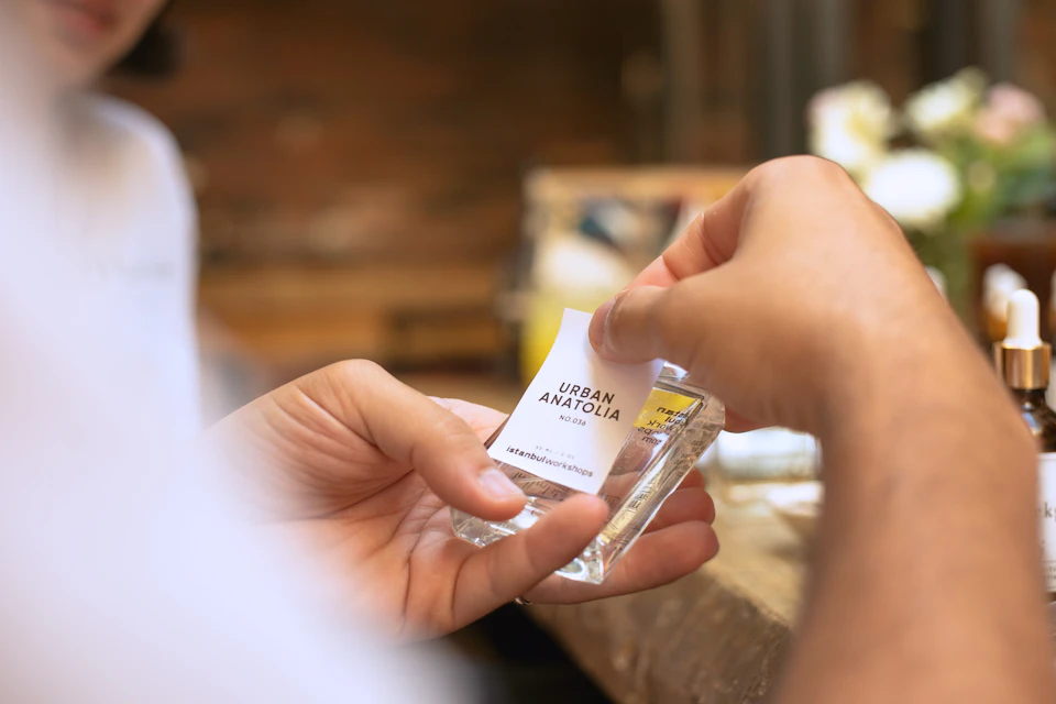 A participant applying a custom label to a perfume bottle labeled "Urban Anatolia" during a workshop.