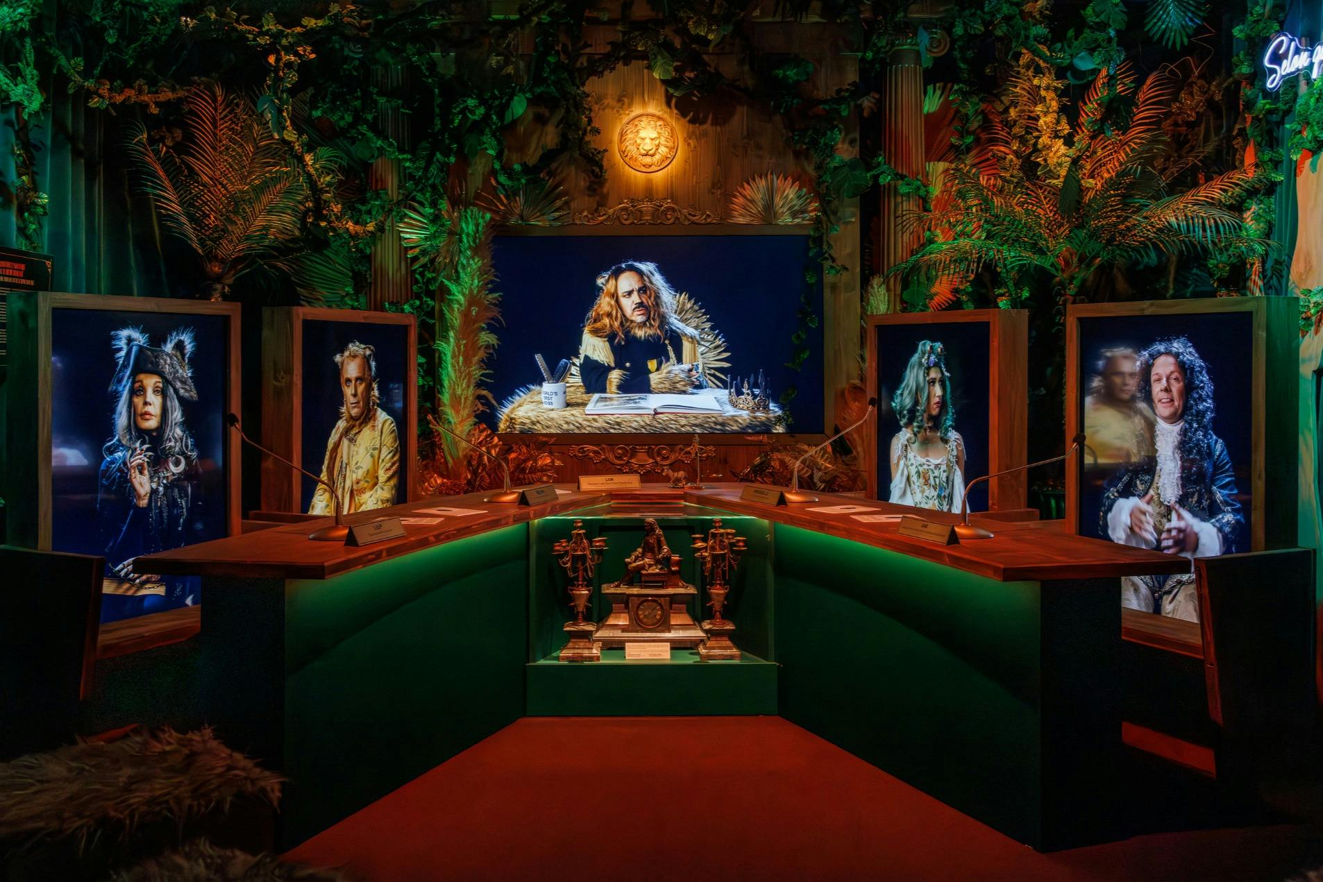 Habitació amb un escriptori amb llum verda, retrats emmarcats de figures històriques i una frondosa vegetació de fons.