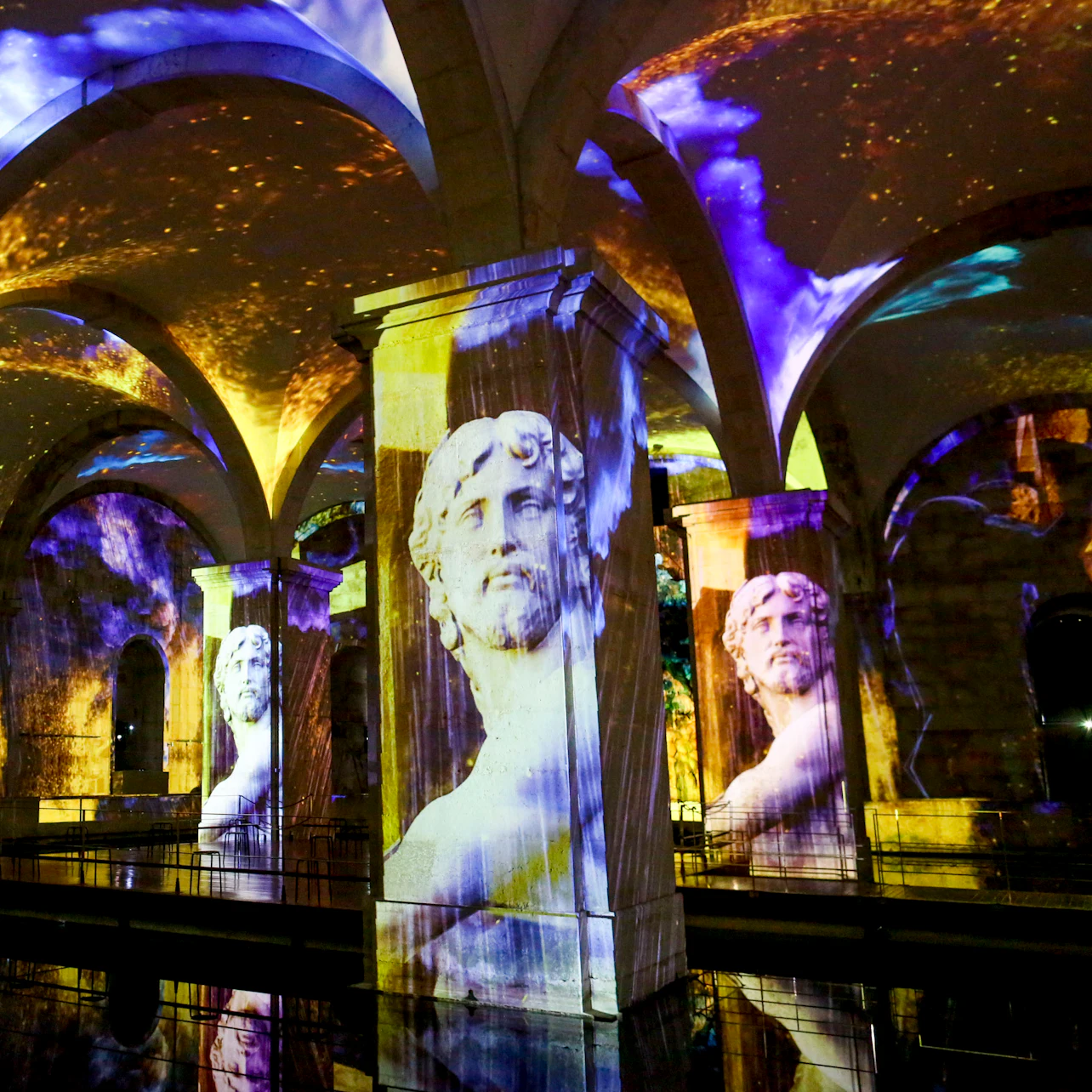 Arched hall with projected images of classical busts and colorful lights reflecting off a glossy floor.