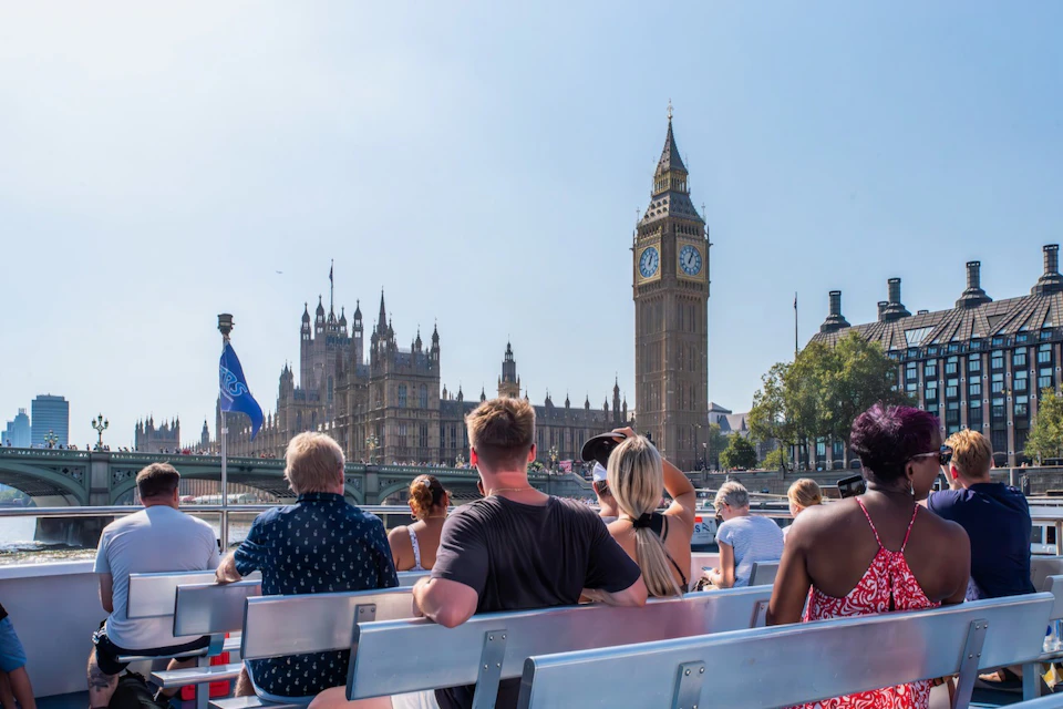 Tourists on a boat viewing Big Ben and the Houses of Parliament under a clear sky in London.