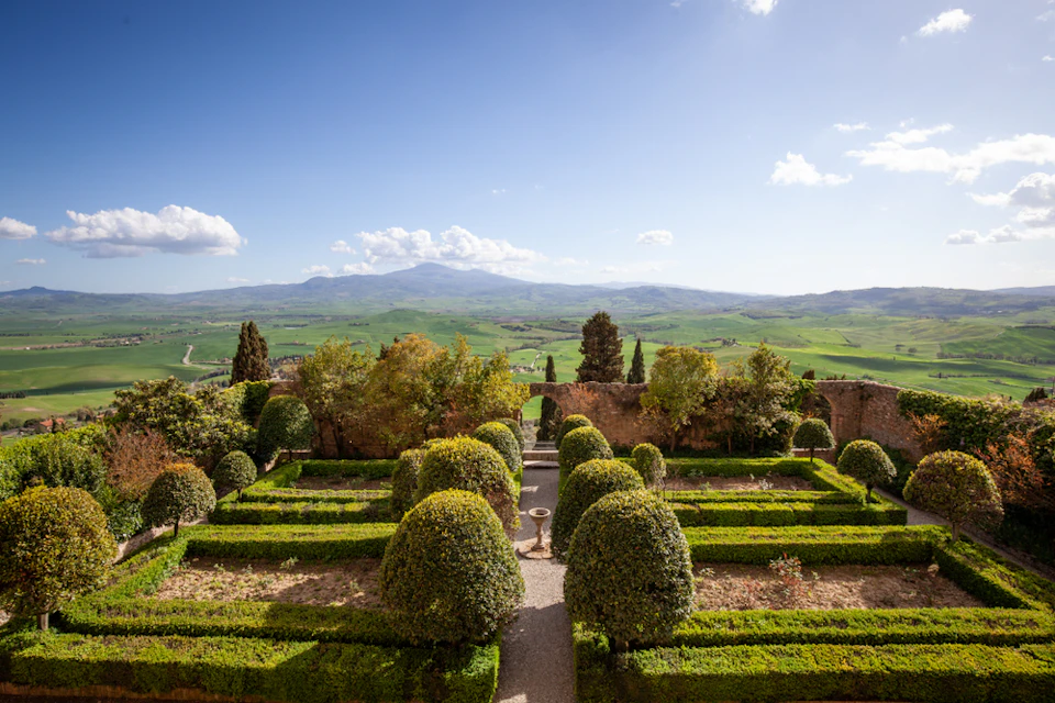 Well-maintained garden with manicured shrubs and hedges, set against a backdrop of rolling green hills and a blue sky.
