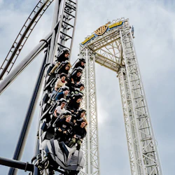 Människor som åker en upphängd berg- och dalbana med uttryck av spänning. En Warner Bros.-logotyp syns i bakgrunden.