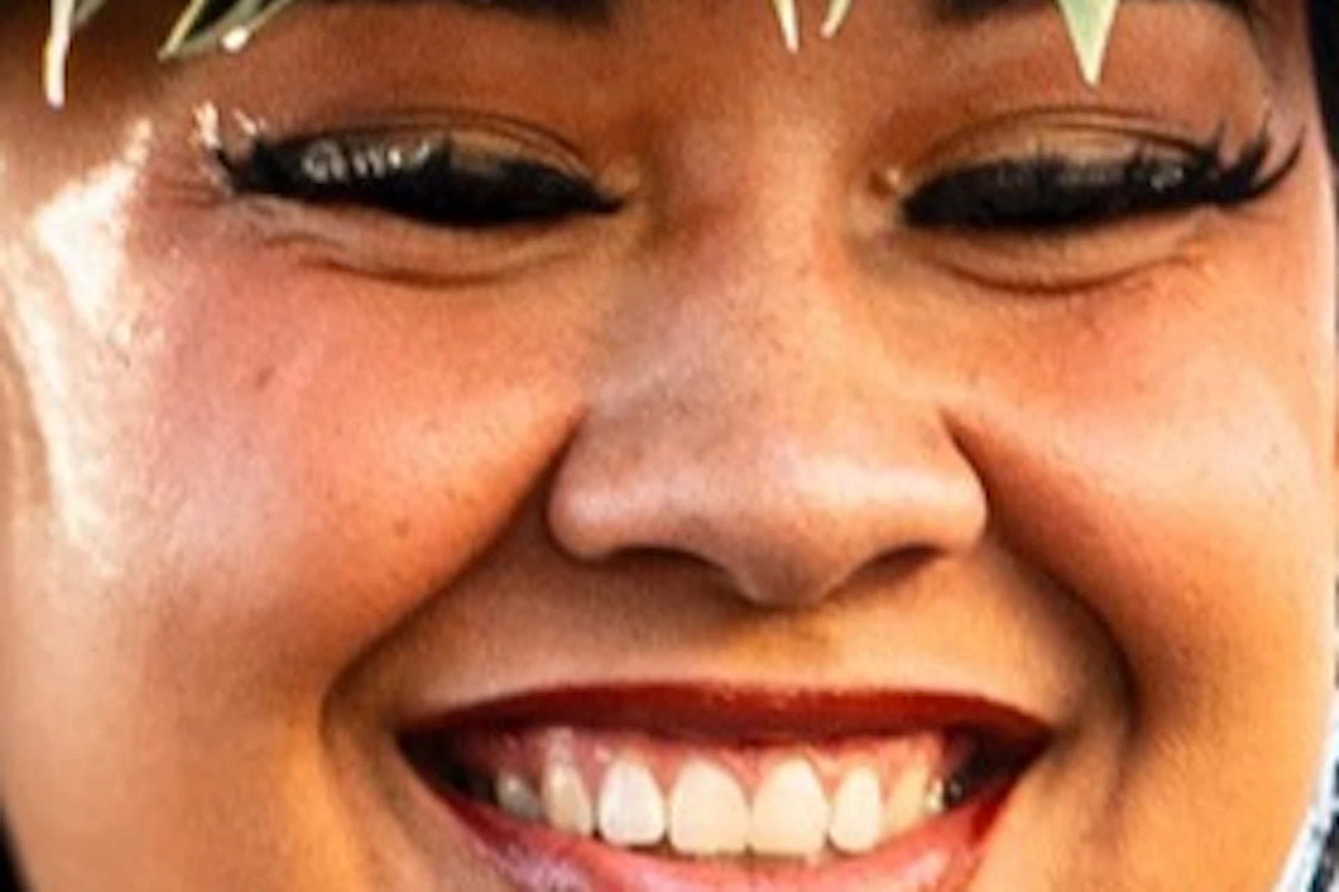 A woman wearing traditional Polynesian attire and a floral headpiece performing a dance outdoors, smiling at the camera.