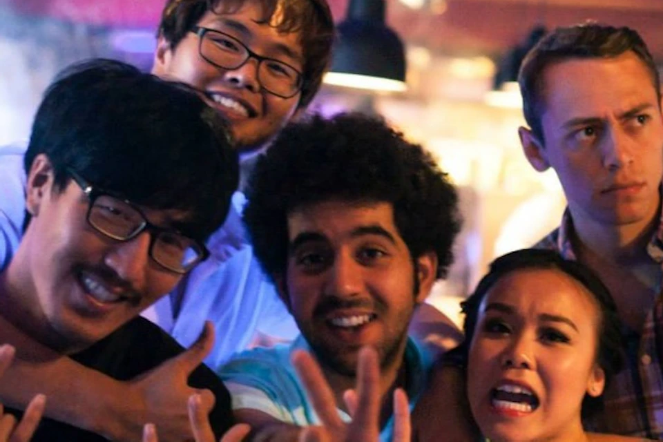 A group of friends smiling and posing for a photo in a lively indoor setting with drinks in their hands.