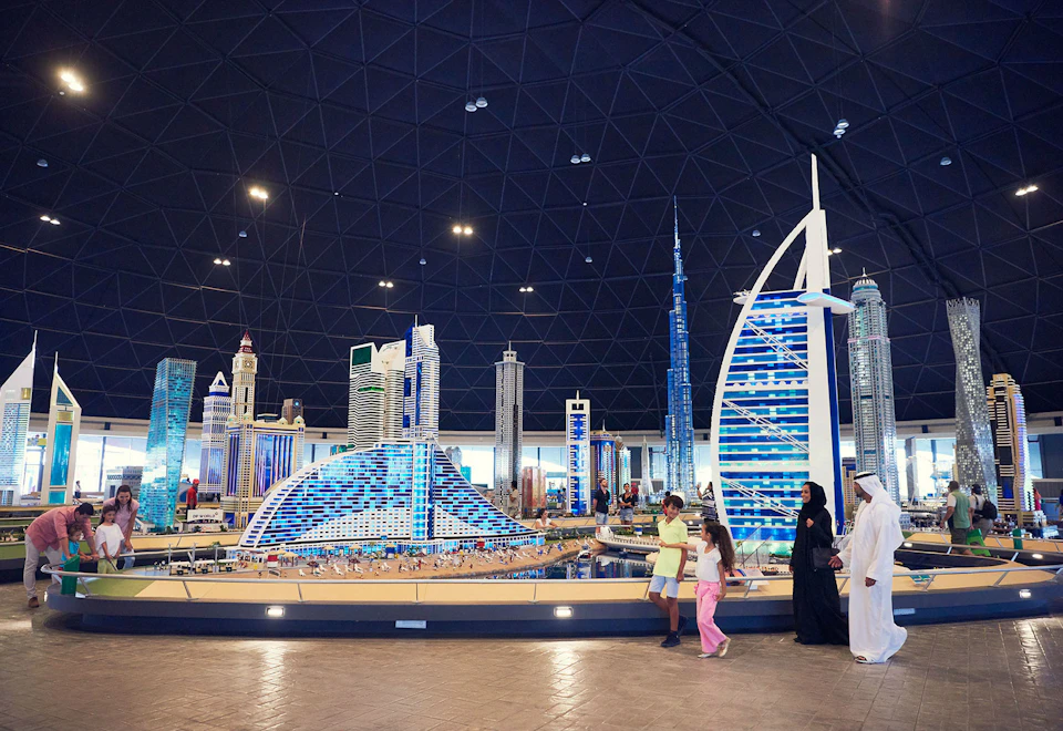 People walking by a detailed Lego model of a city's skyline, including iconic skyscrapers, inside a dome structure.