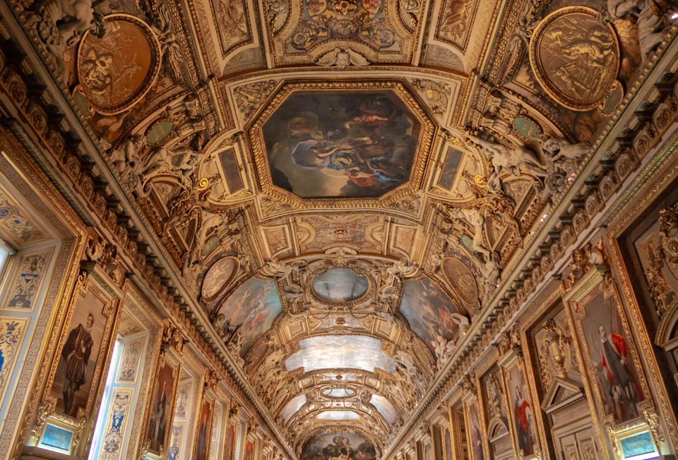 Ornately decorated ceiling with intricate paintings and sculptures in a grand architectural interior space.