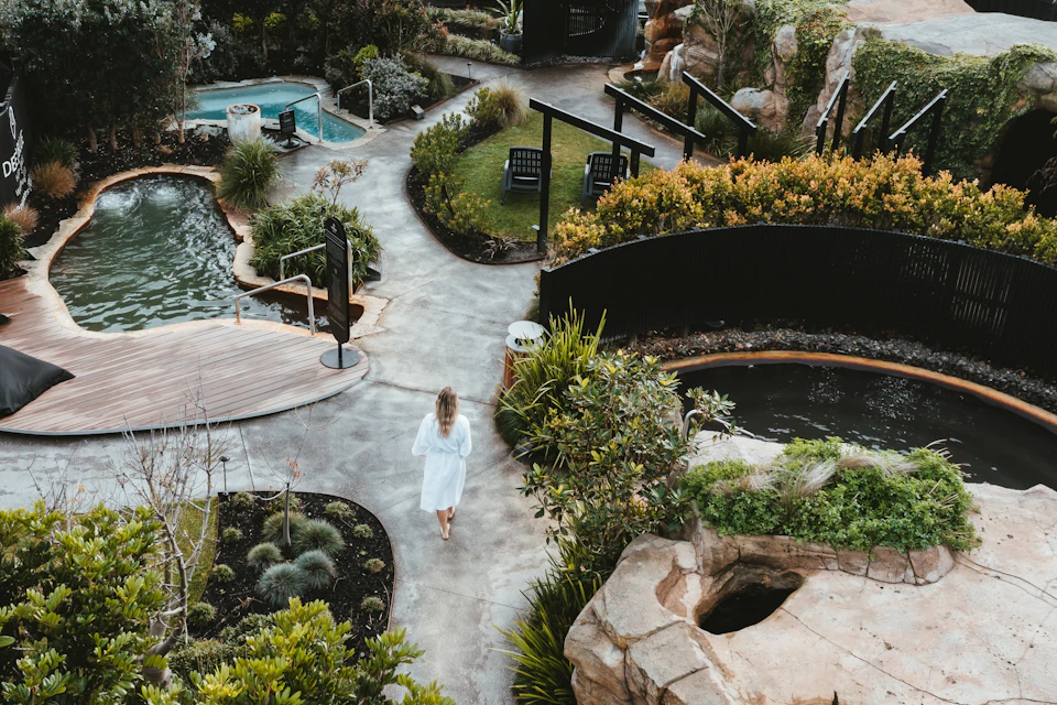 Aerial view of woman wandering in sanctuary with numerous paths, geothermal rockpools, caves, and cold plunge pool.